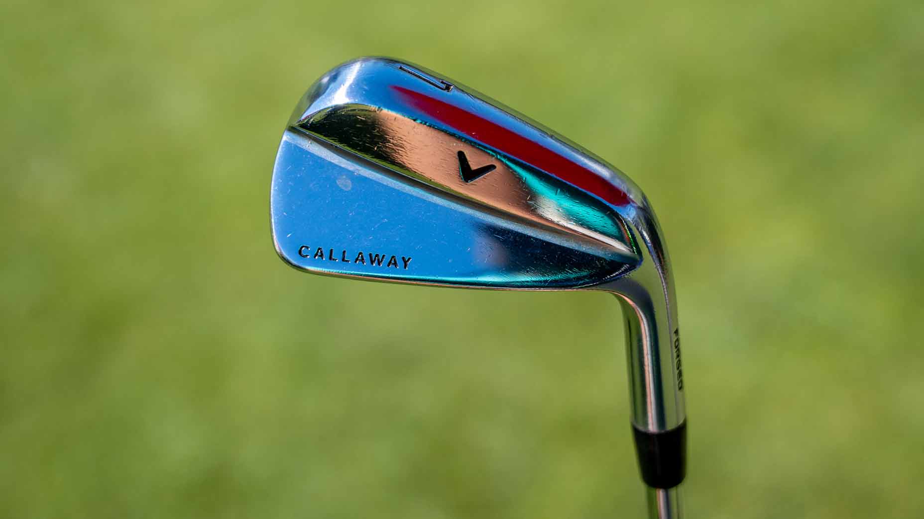 A close-up of a shiny Callaway golf iron, similar to those favored by Collin Morikawa during The Open, with a reflective surface set against a blurred green background.