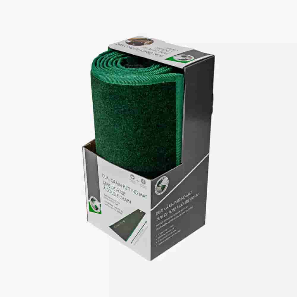 A rolled-up green dual grain putting mat displayed upright in its original black and white packaging, with part of the mat visible and product details printed on the box&mdash;an ideal companion for those seeking the best golf bags 2026.
