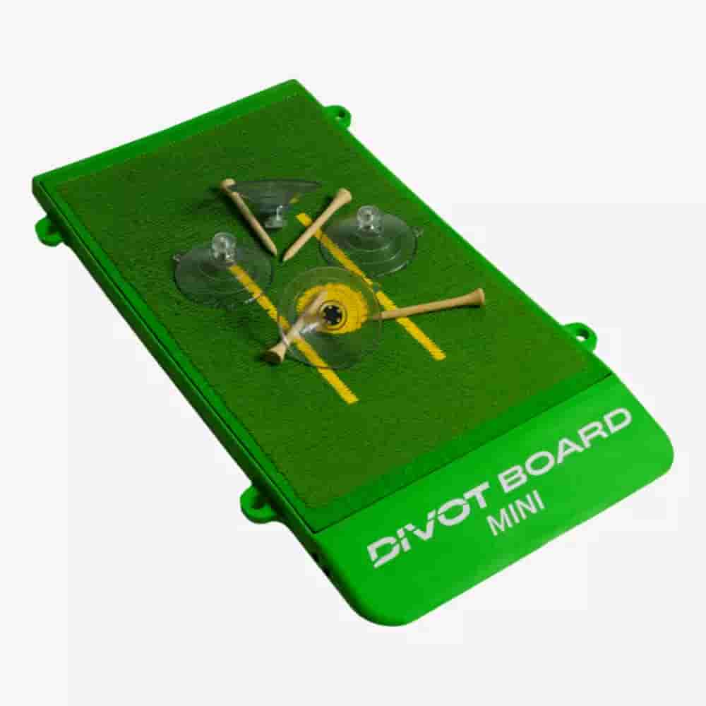A green rectangular Divot Board Mini with artificial turf, yellow alignment lines, two suction cups, golf tees, and DIVOT BOARD MINI printed on the side&mdash;an ideal practice companion for those searching for the best golf bags 2026.
