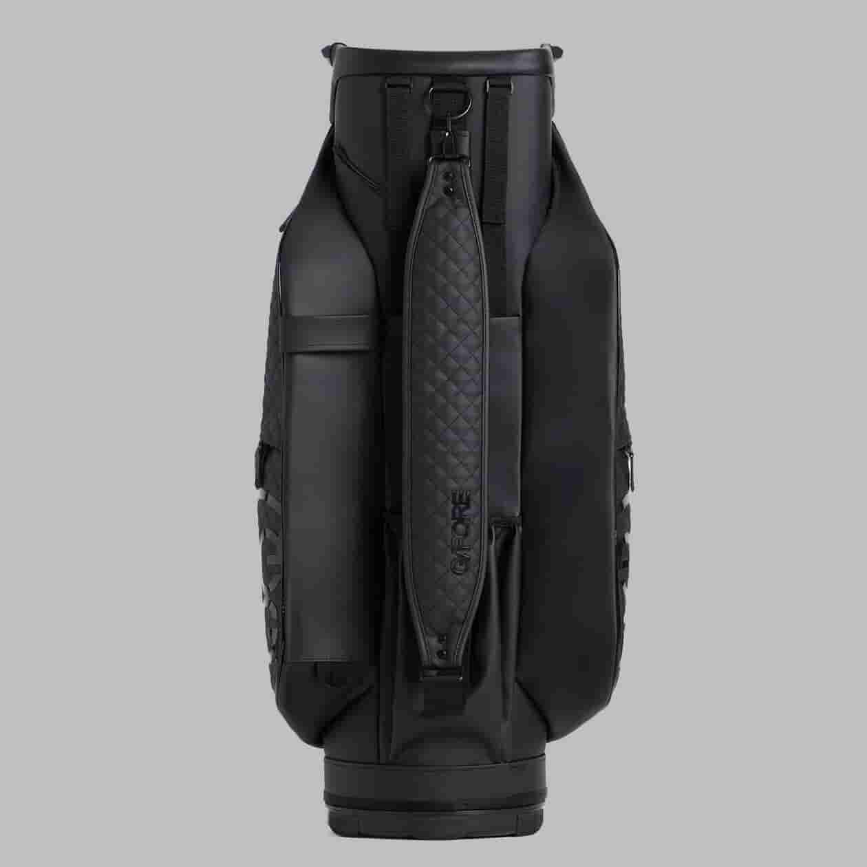 A black golf bag with a textured, padded shoulder strap stands upright against a plain gray background. With multiple compartments and a sleek, modern design, it&rsquo;s set to be one of the best golf bags 2026 has to offer.