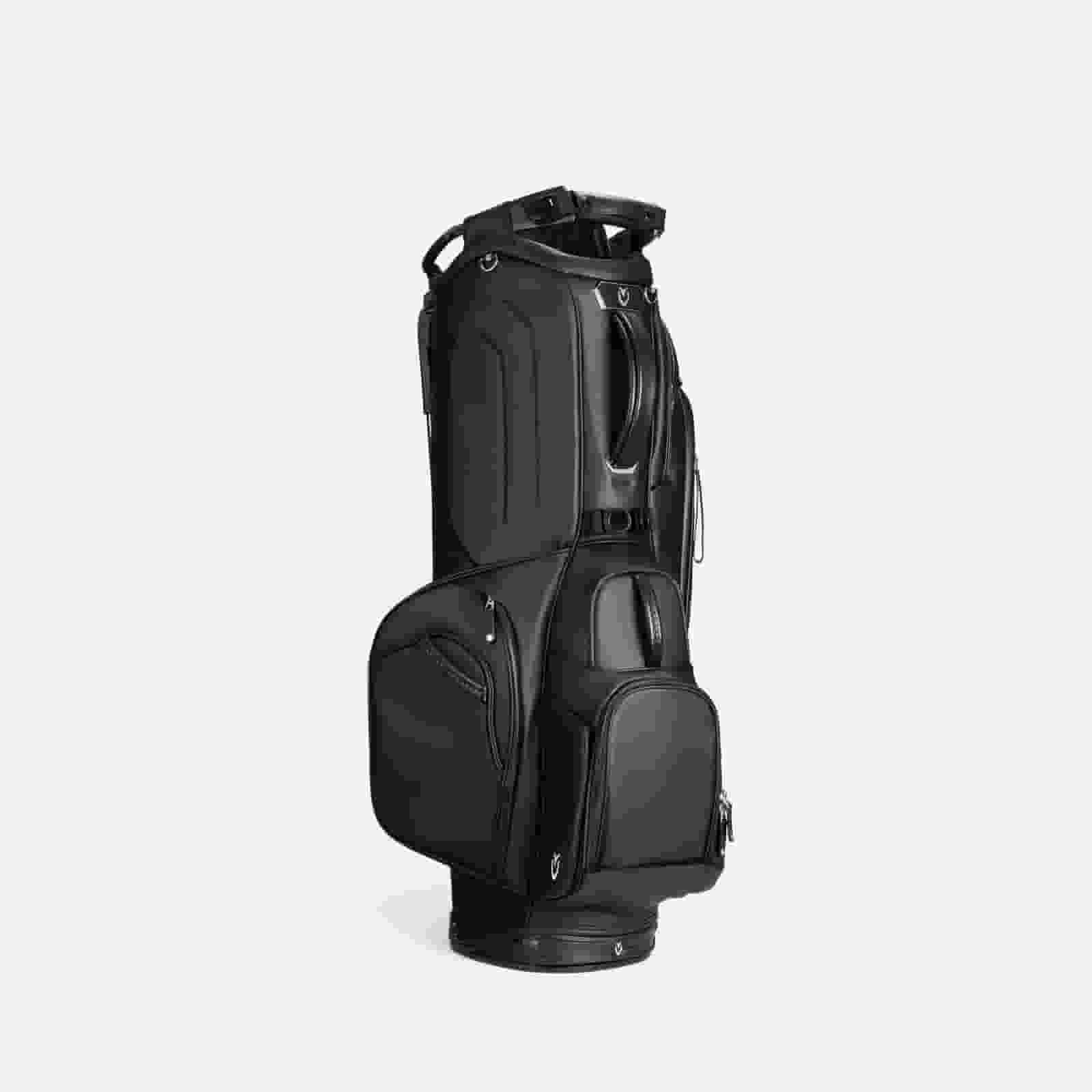 A black golf bag with multiple zippered pockets and compartments stands upright against a plain, light gray background&mdash;an ideal choice for those seeking the best golf bags 2026 has to offer.