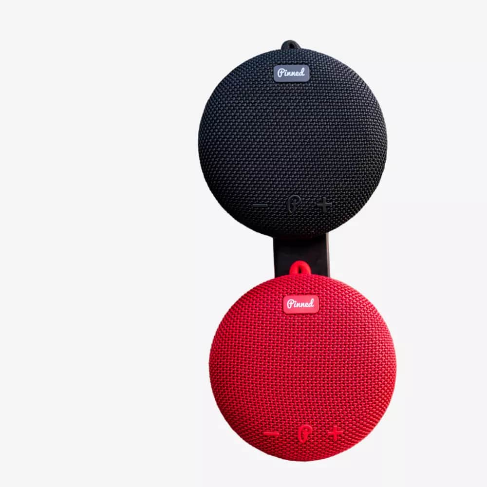Two round, portable wireless speakers, one black and one red, are stacked vertically against a white background. Both feature fabric textures, control buttons, and the brand logo&mdash;perfect for those seeking the best deals under $50.