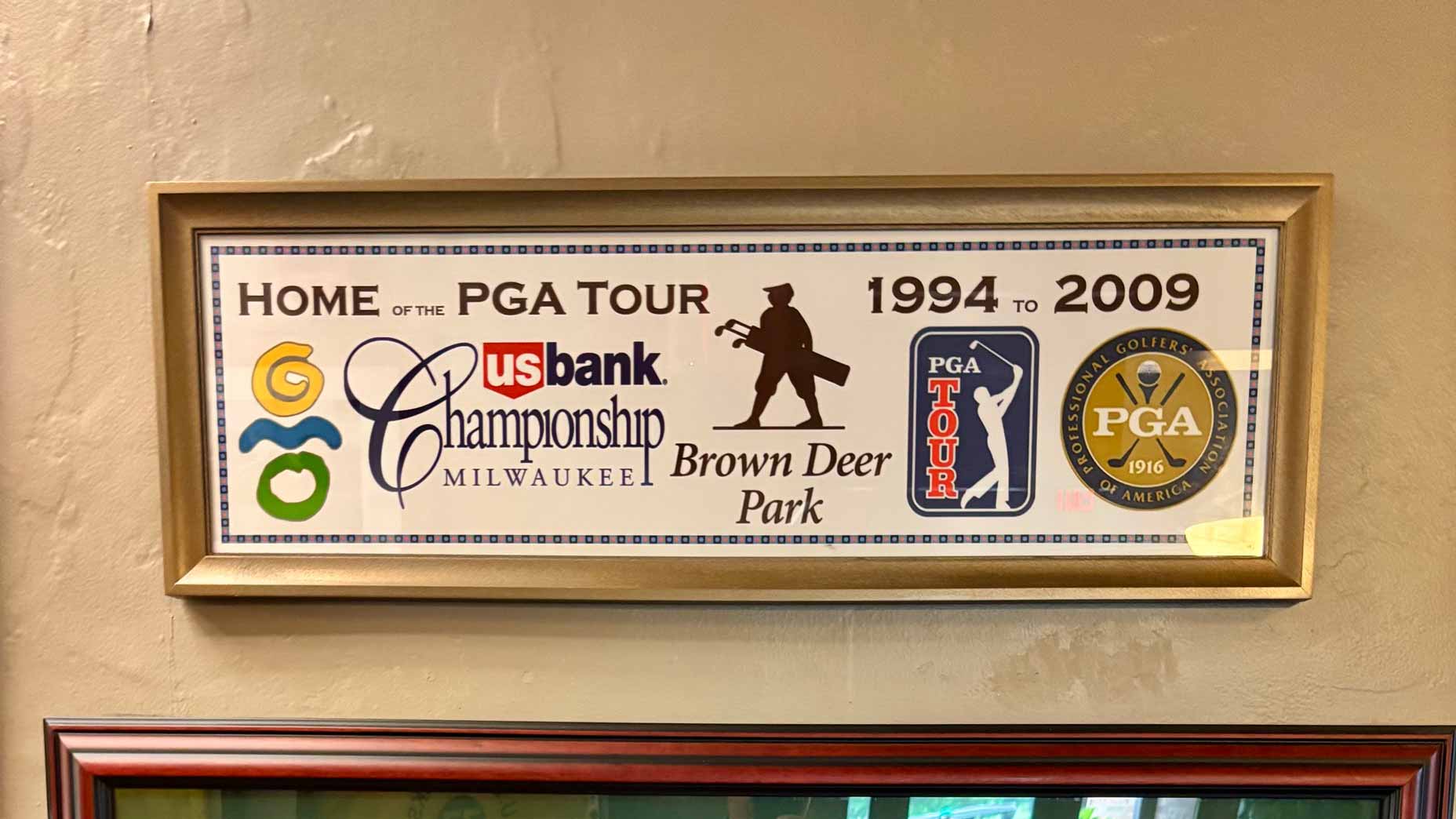 Framed sign reading Home of the PGA Tour 1994 to 2009 with logos for US Bank Championship Milwaukee, Brown Deer Park, PGA Tour, and PGA of America on a beige wall&mdash;an ideal inspiration piece for anyone planning an affordable golf vacation or memorable Wisconsin golf trip.