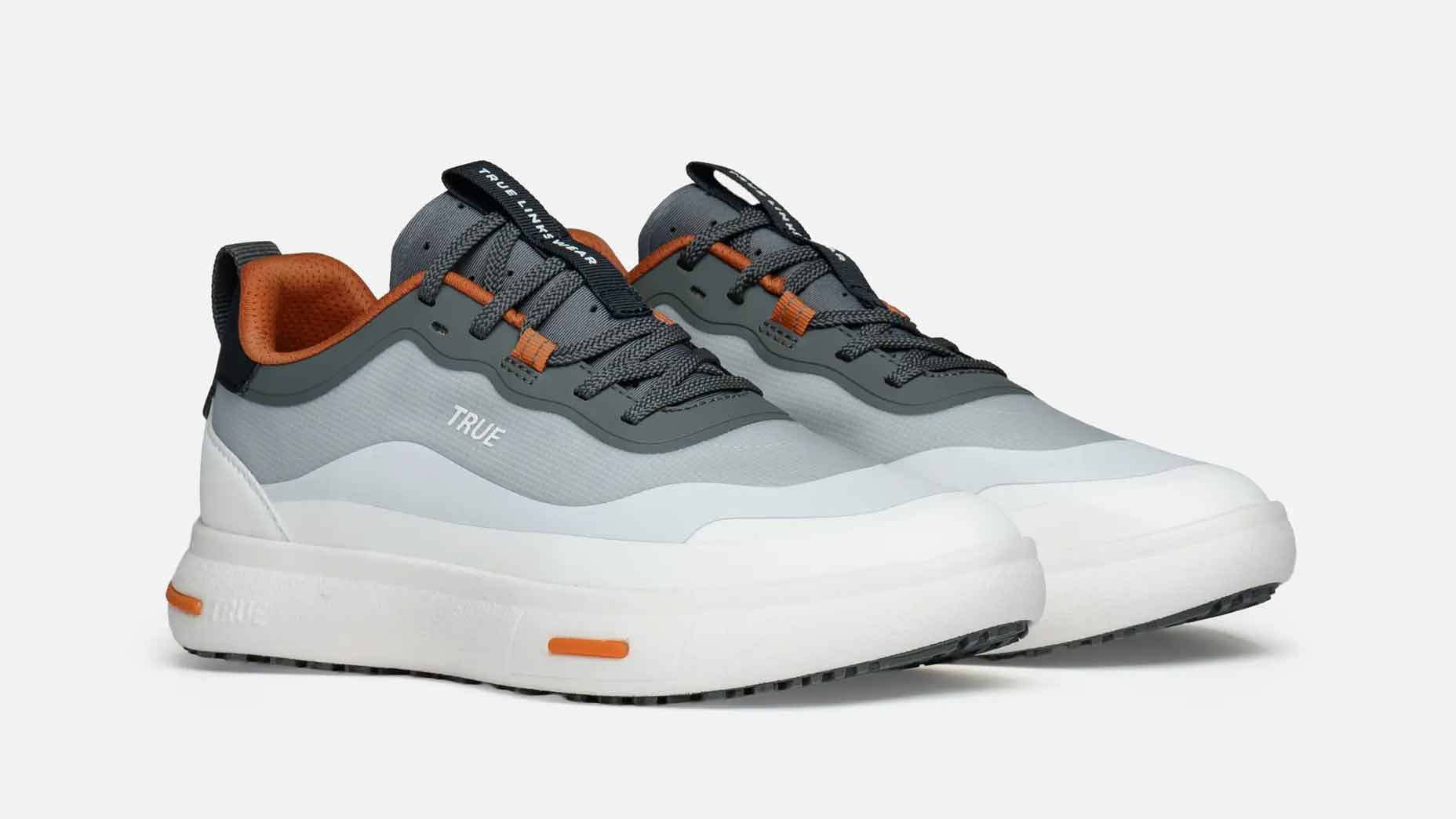 A pair of modern, low-top True Linkswear golf shoes in shades of white, gray, and orange, featuring thick white soles, gray laces, and orange accents&mdash;perfect as comfortable golf shoes&mdash;placed on a plain white background.