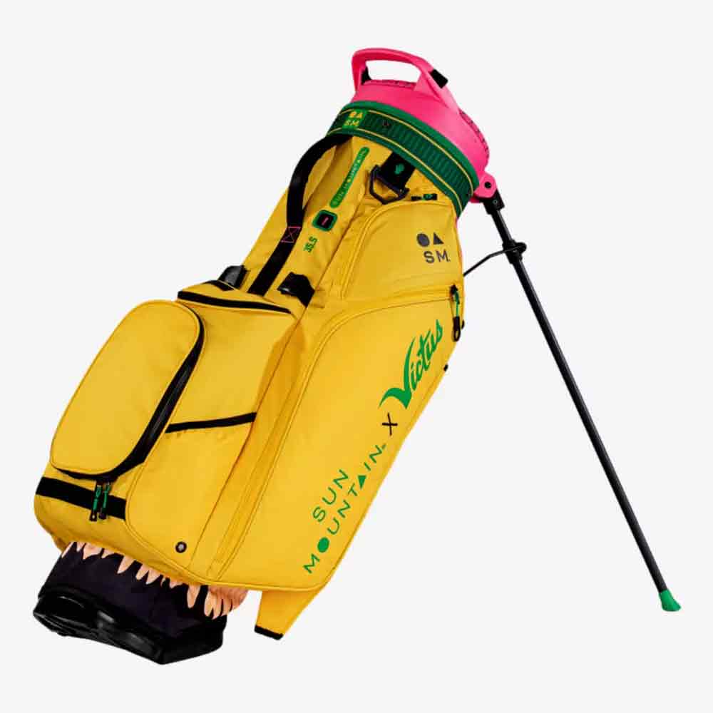 A vibrant Sun Mountain golf bag with green accents, a pink handle, and a black stand. One pocket features teeth and a pink interior, resembling a mouth. &ldquo;Sun Mountain X Victus&rdquo; is boldly displayed on the side.