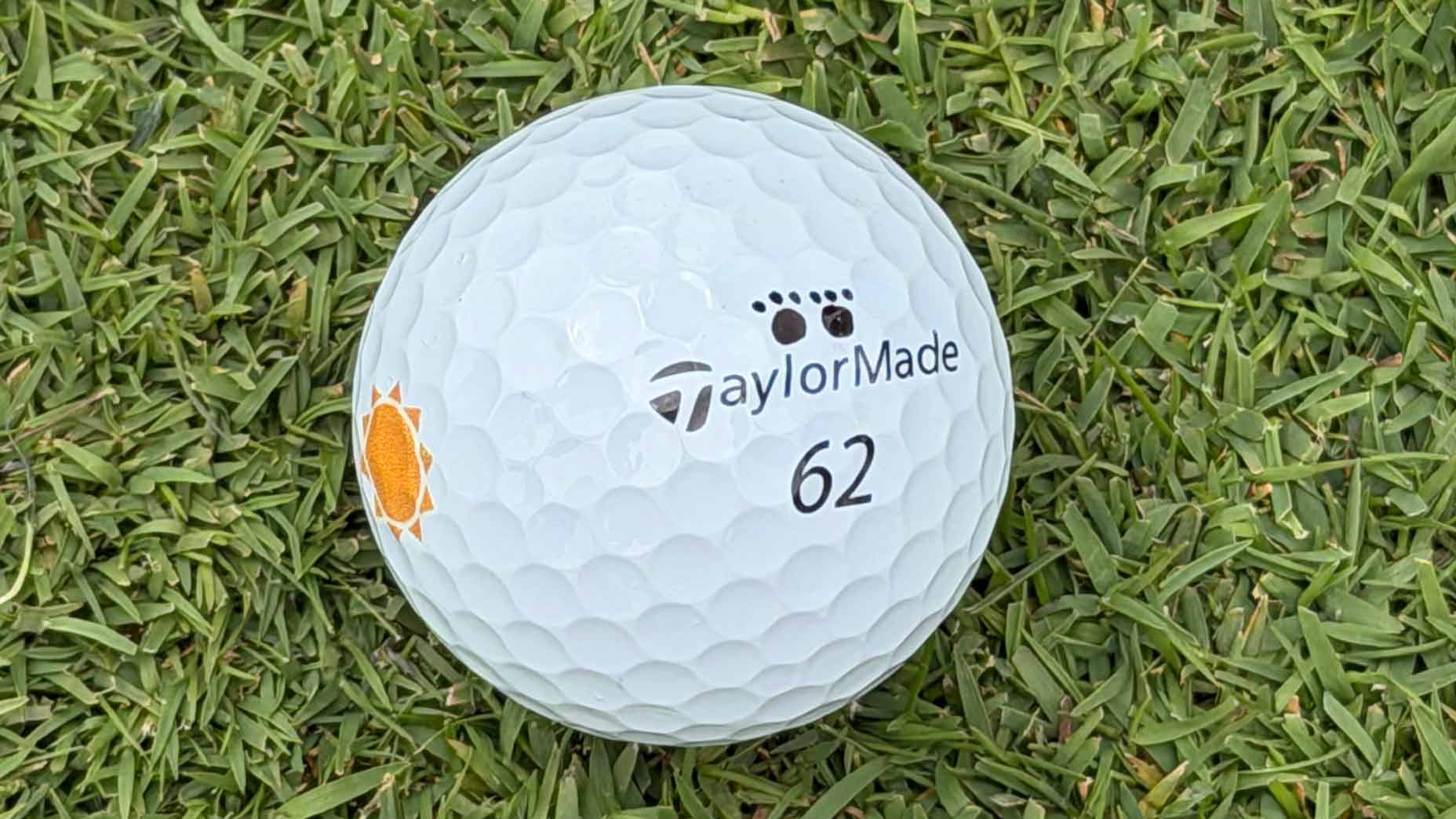 A white TaylorMade golf ball marked with the number 62 and an orange graphic, often seen in WITB features, rests on green grass.