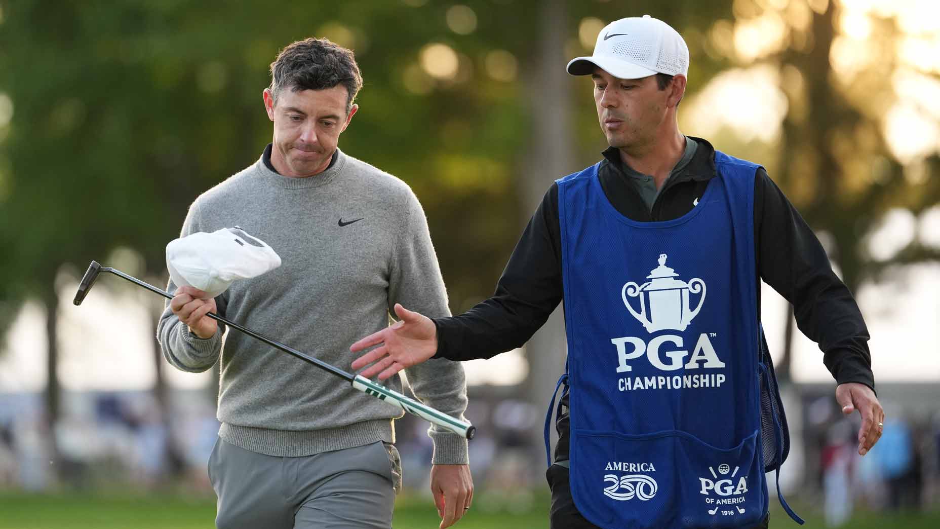 Rory McIlroy hands his putter to his caddie while walking during the second round of 2026 PGA Championship at Aronimink.