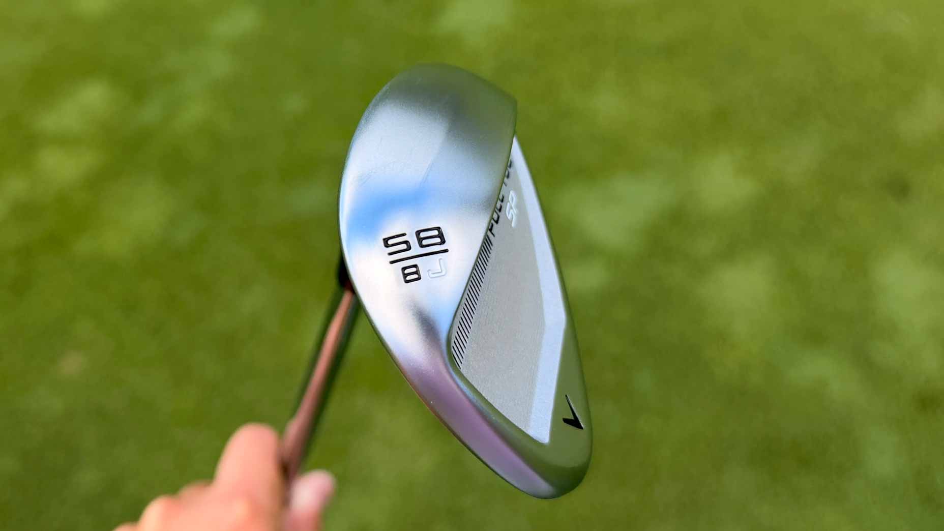 A close-up of a silver Callaway Full Toe golf wedge, showing the numbers 58 and 8 on its head, held over a blurred green grass background.