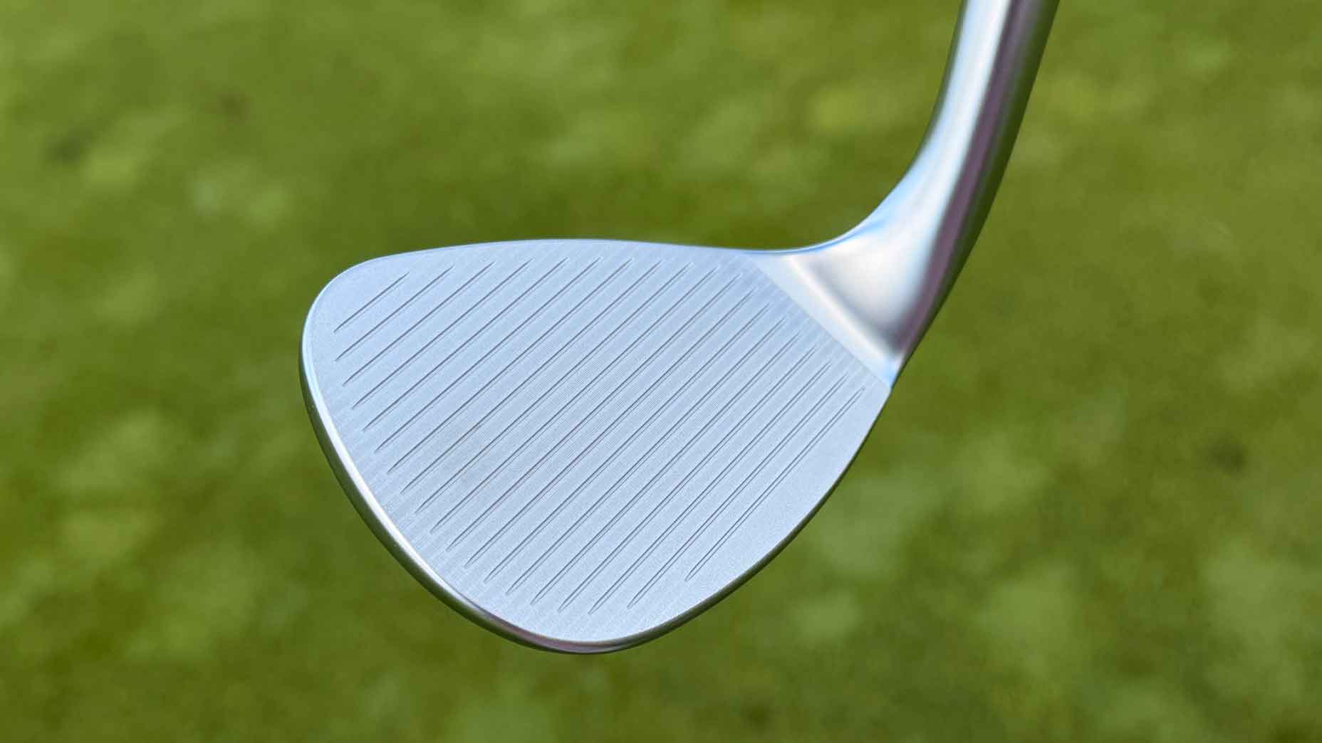 Close-up of a clean, silver Callaway Full Toe golf club wedge head with visible grooves, set against a blurred green grass background.