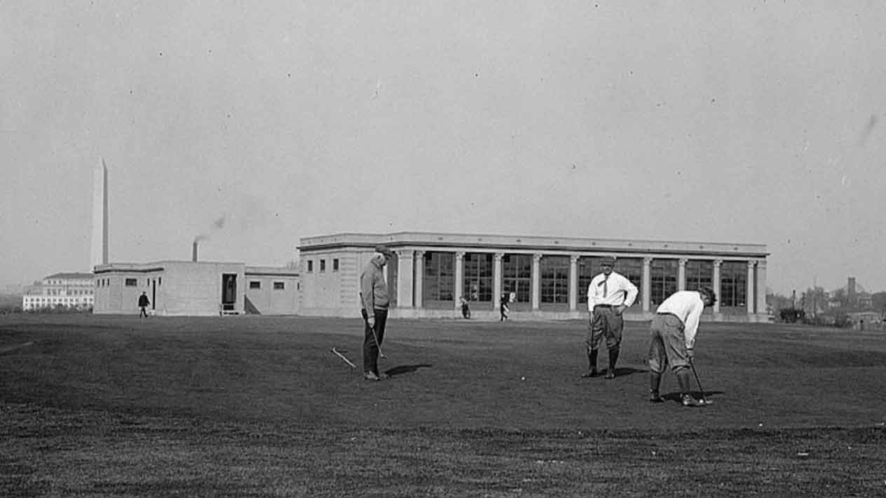 Three men play golf on a grassy course with a large building in the background. The Washington Monument is visible in the distance, highlighting this D.C. muni-golf project under a clear sky.