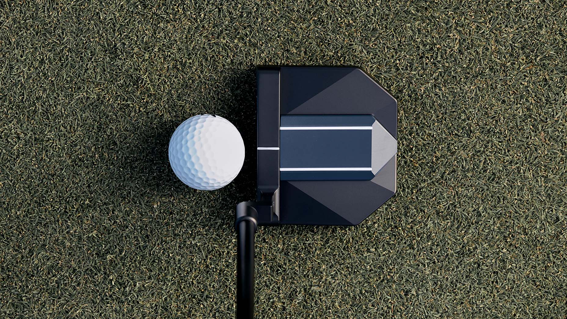 A close-up top view of a golf ball positioned next to a black putter on a grass surface, ready for a putt.