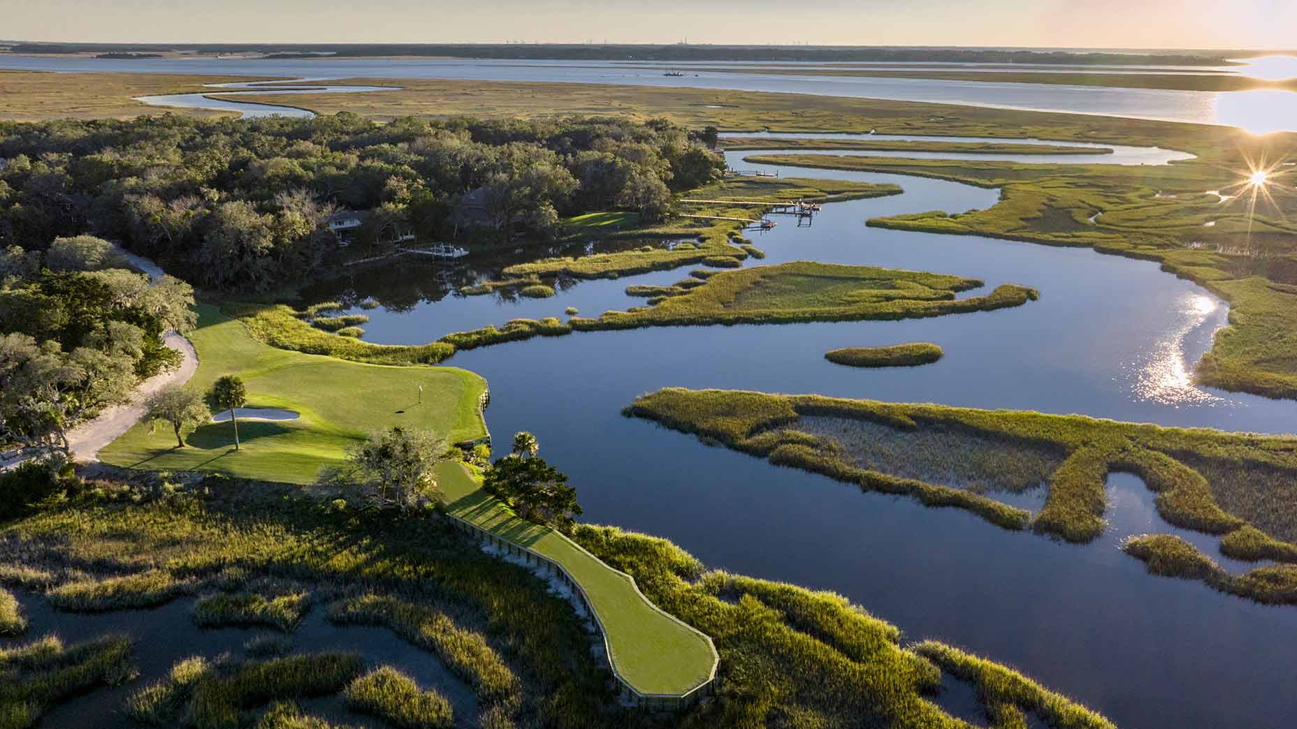Aerial view of Omni Amelia Island Resort&rsquo;s lush golf course, perfect for a buddies' trip getaway, surrounded by winding water channels, marshland, and greenery with sunlight reflecting off the water and a distant treeline.