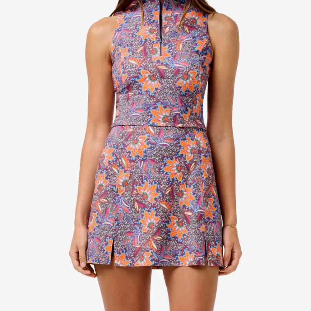 A woman wearing a sleeveless, high-neck, floral dress with a colorful pattern in purple, orange, and pink&mdash;a stylish choice for Mother&rsquo;s Day. The dress features a fitted waist and short hemline with small front slits.