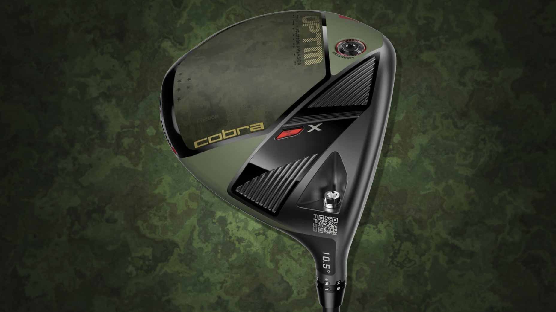 A close-up of a Cobra golf driver with a black and olive green volition design, featuring the brand name and a QR code on the clubhead, set against a camouflage-patterned background.