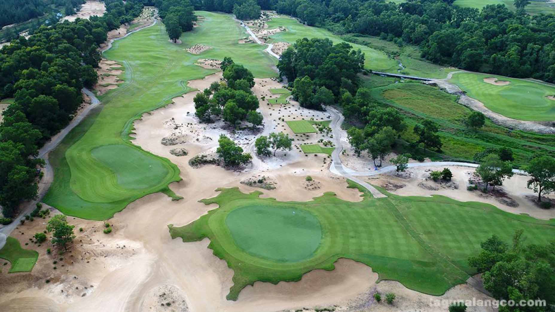 Aerial view of Banyan Golf Club Hua Hin, one of the top 100 golf resorts, with lush green fairways, sand bunkers, trees, winding paths, and patches of sandy terrain surrounded by dense forest.