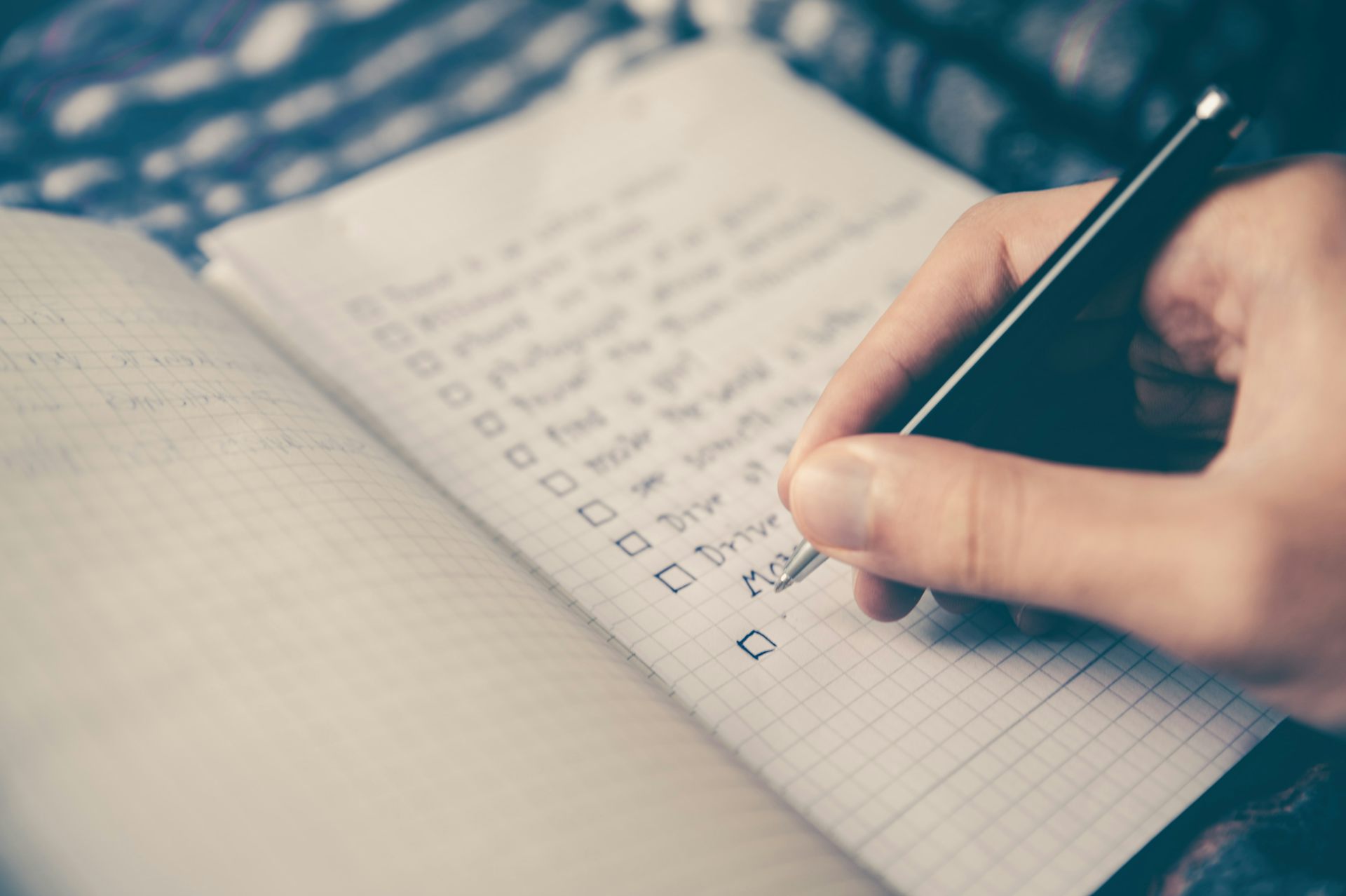 Hand using pen to write checklist on notebook.