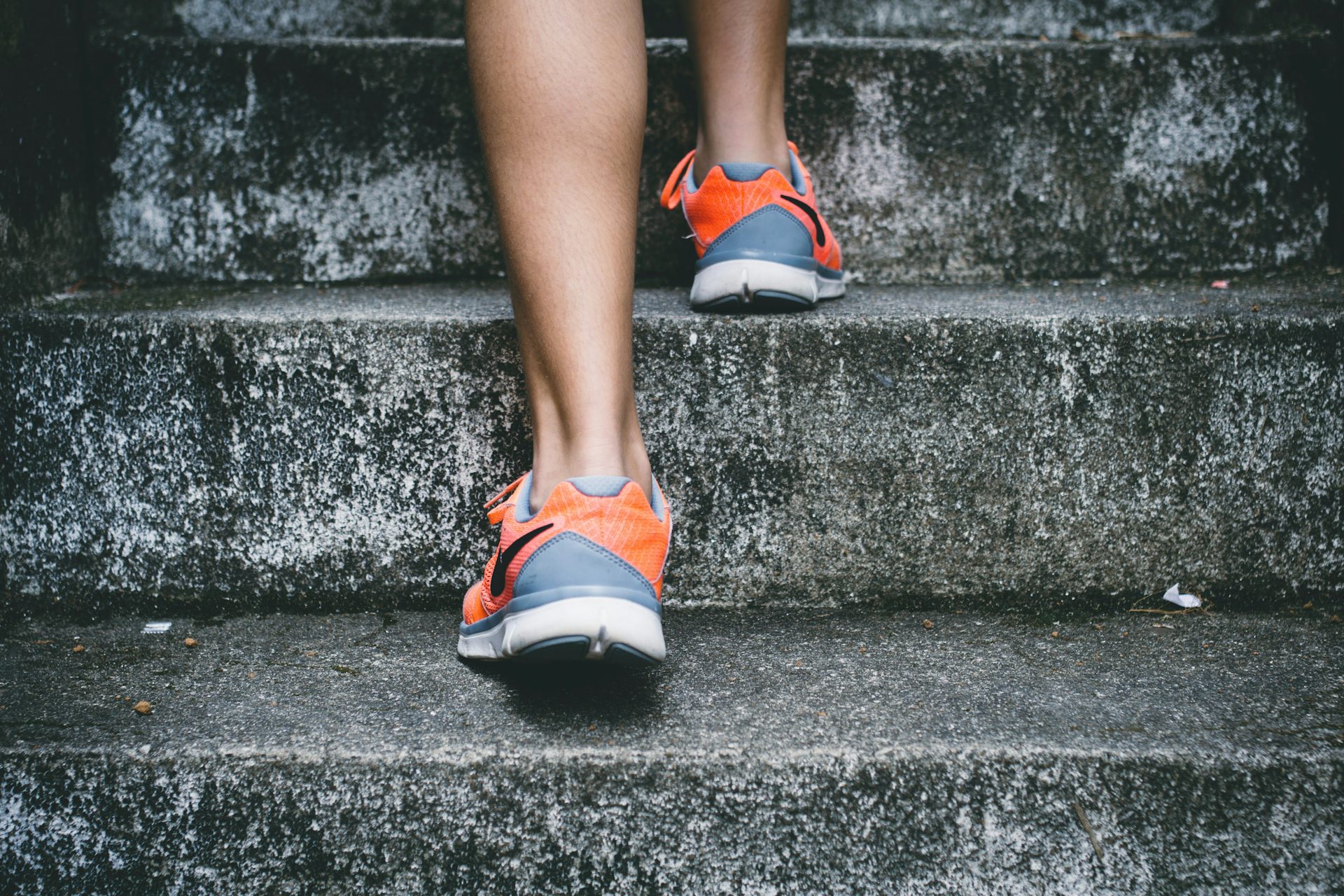 Legs of someone wearing orange and gray shoes walking up concrete steps.